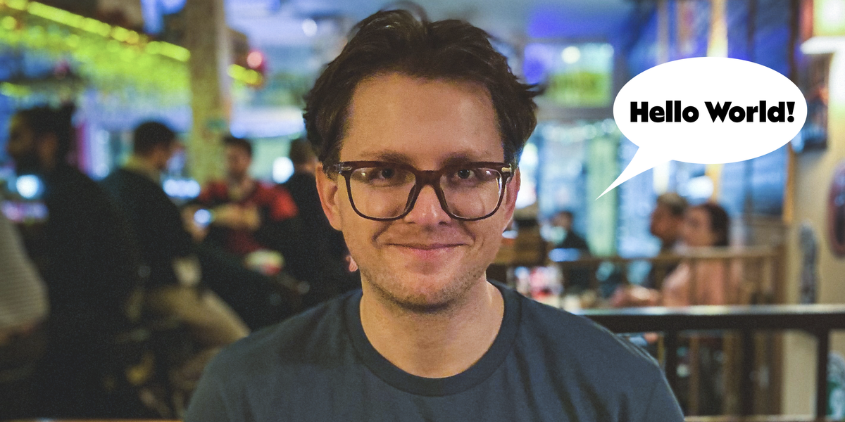 Jürgen with messy hear, grinning wide. There's a speech bubble next to his face that says "Hello World!". The background is blurred but we can see it's a bar.