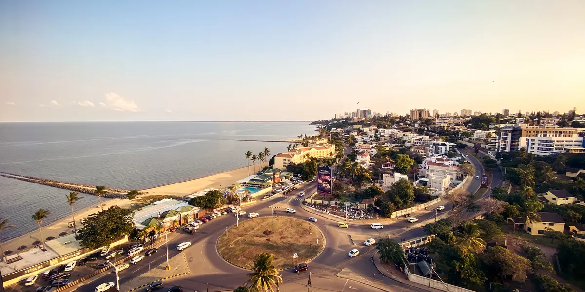The view from my hotel room – Maputo's coastline at golden hour. A large roundabout and a palm-lined beach sit between the road and the Indian Ocean, with the city's high-rises receding into the haze along the shore.