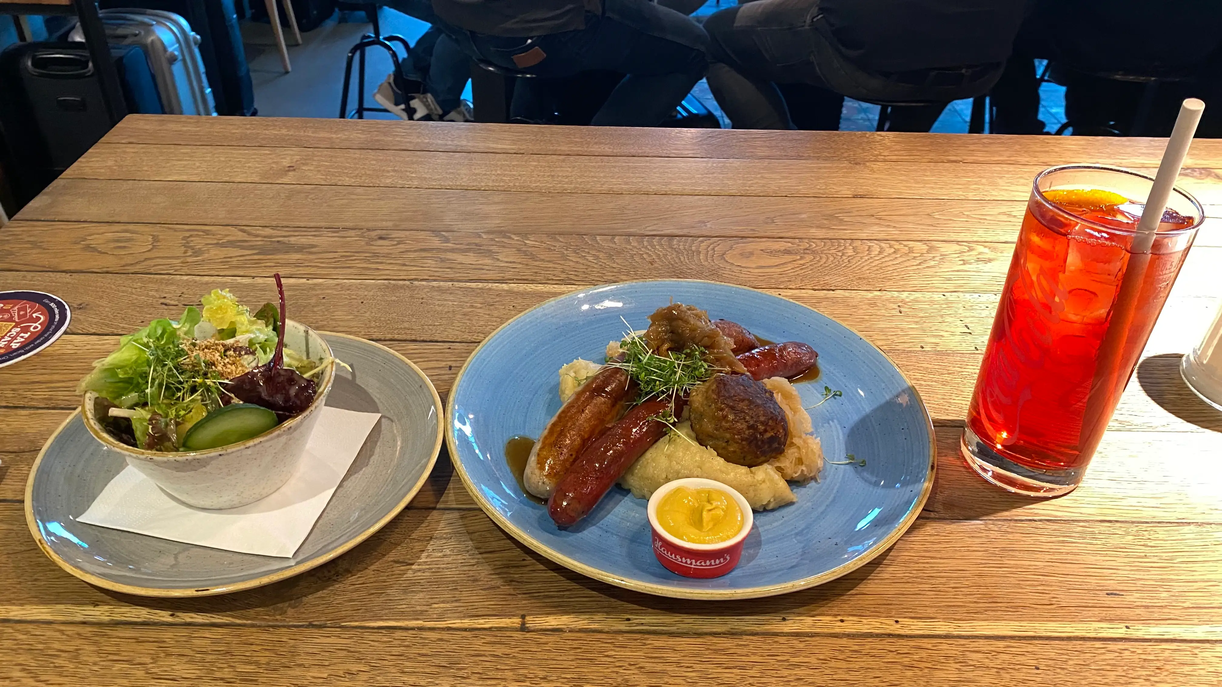 On the left of the table, there is a small salad bowl. In the middle some mashed potatoes, meatballs and sausages, with a mustard sauce bowl. On the right, a glass of iced tea.