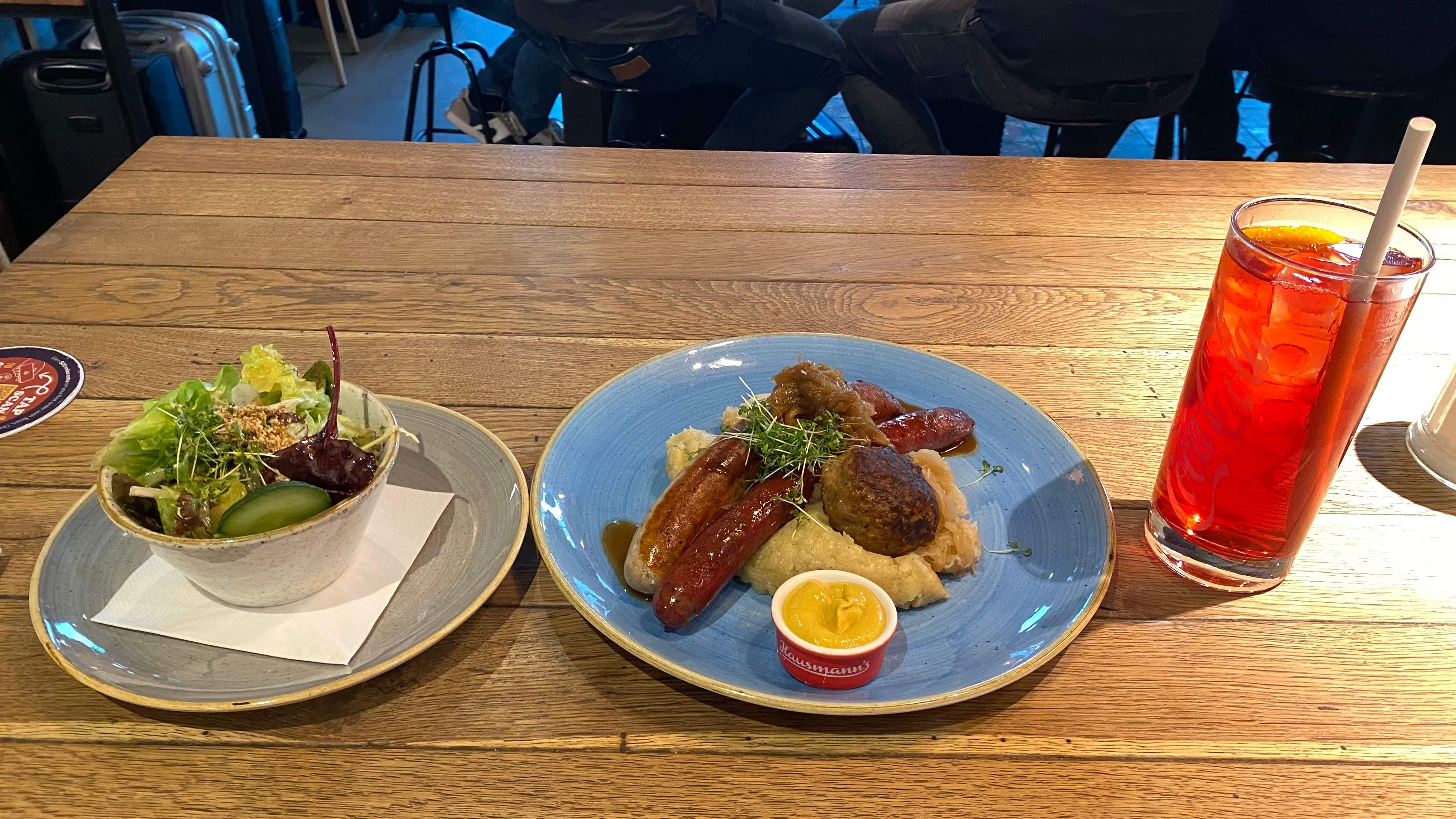 On the left of the table, there is a small salad bowl. In the middle some mashed potatoes, meatballs and sausages, with a mustard sauce bowl. On the right, a glass of iced tea.