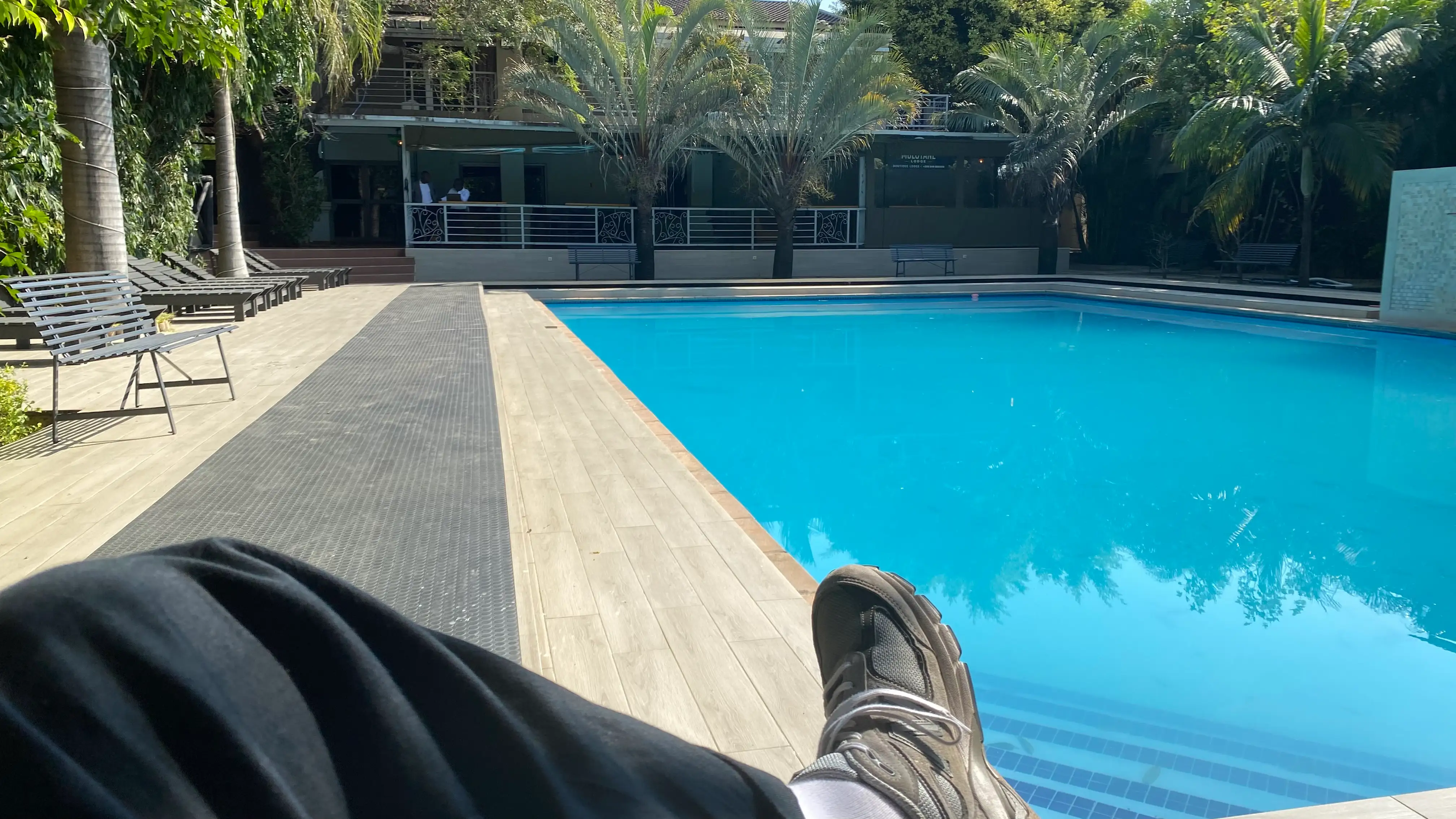 A pool surrounded by tropical trees. In the foreground you can see my leg and sneaker. A rare moment of pause.